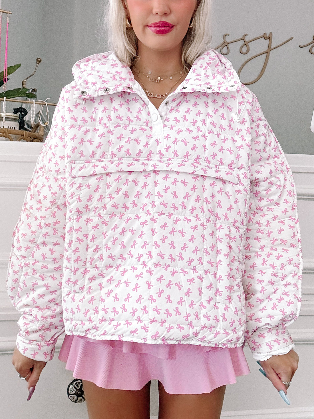 White quilted pullover with pink bow print, shown on model.
