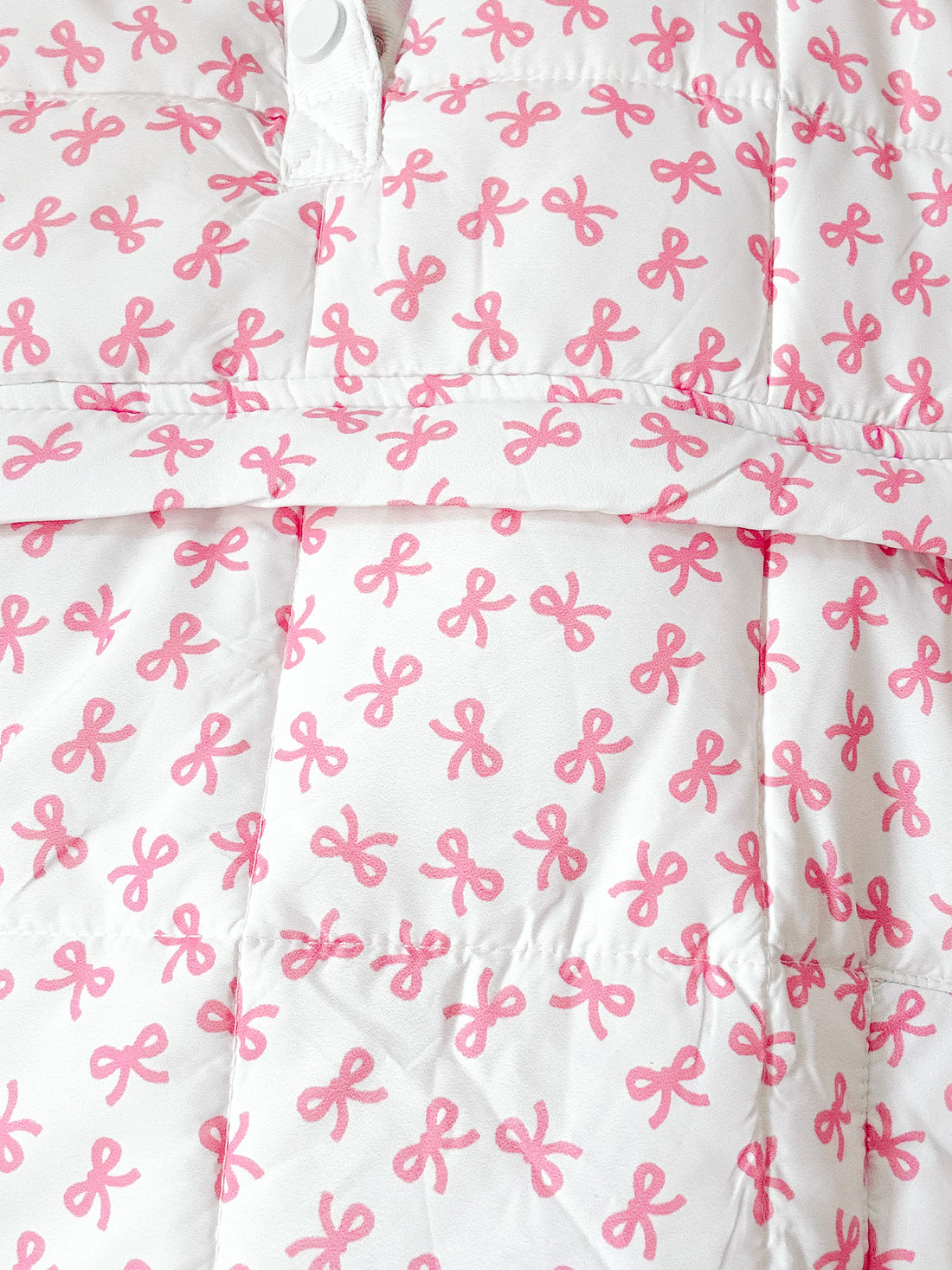 Close-up of white quilted pullover with pink bow pattern.
