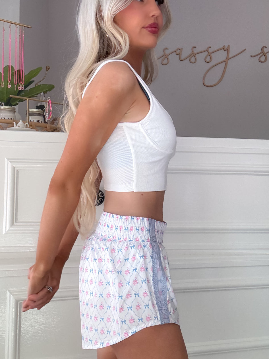White floral shorts with delicate bows, shown on a model against a white wall.
