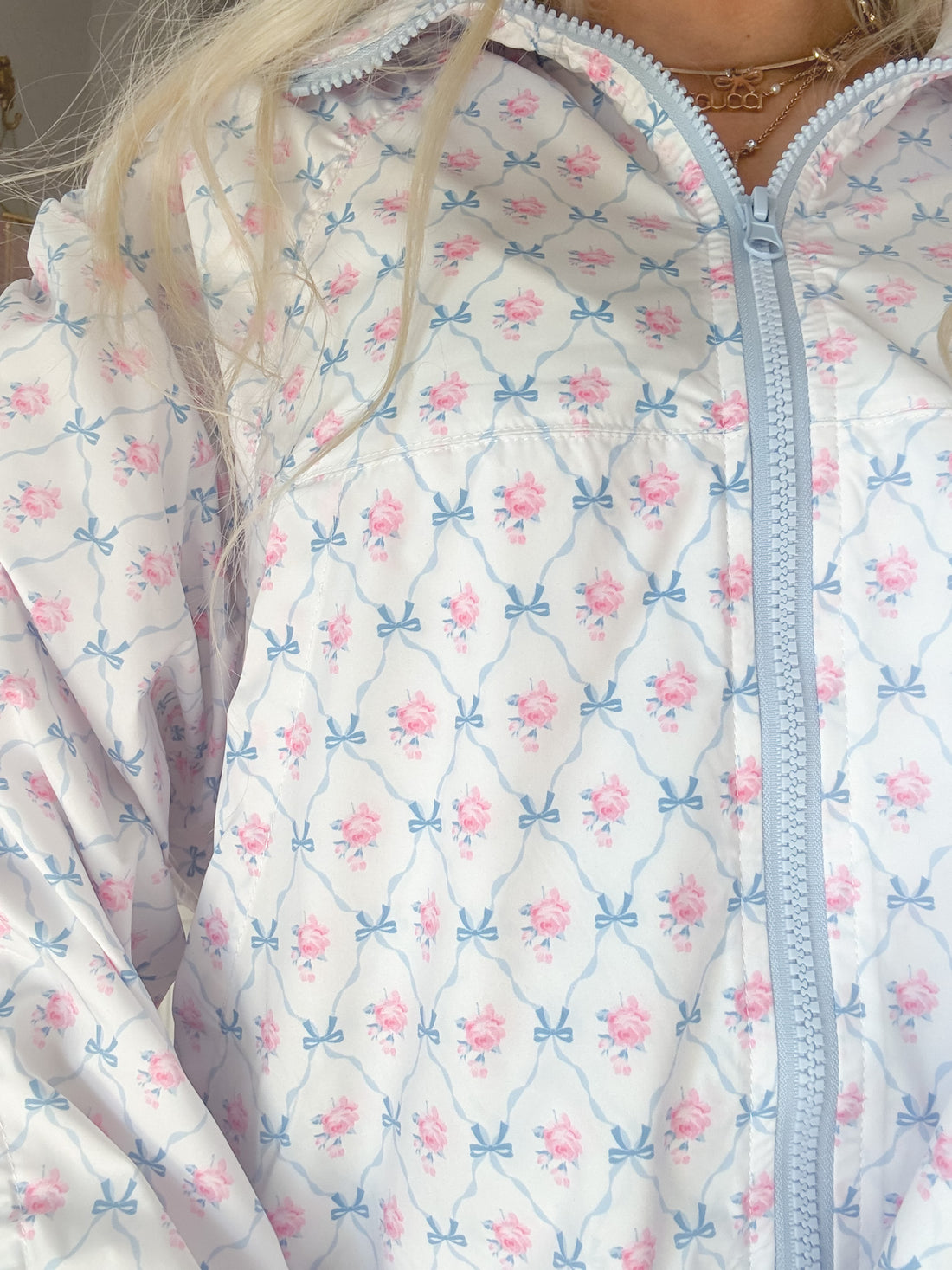 Light blue zip-up windbreaker featuring a delicate pink rose and bow print.
