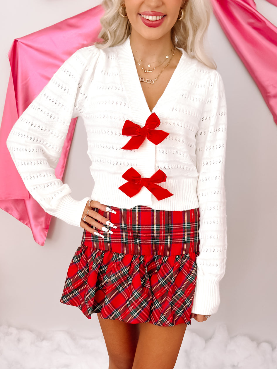 Red and green plaid mini skirt styled with a white knit cardigan; festive holiday outfit.
