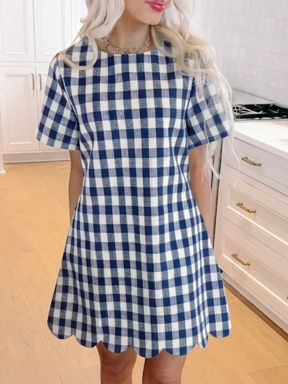 A model wearing the Picnic Princess Gingham Dress in navy blue and white checkered print, featuring short sleeves and a scalloped hem from Sassy Shortcake
