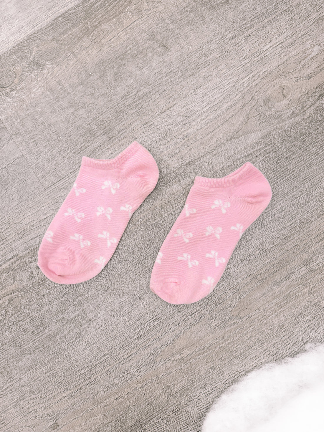 Pink ankle socks with a bow pattern, shown on a wood background.
