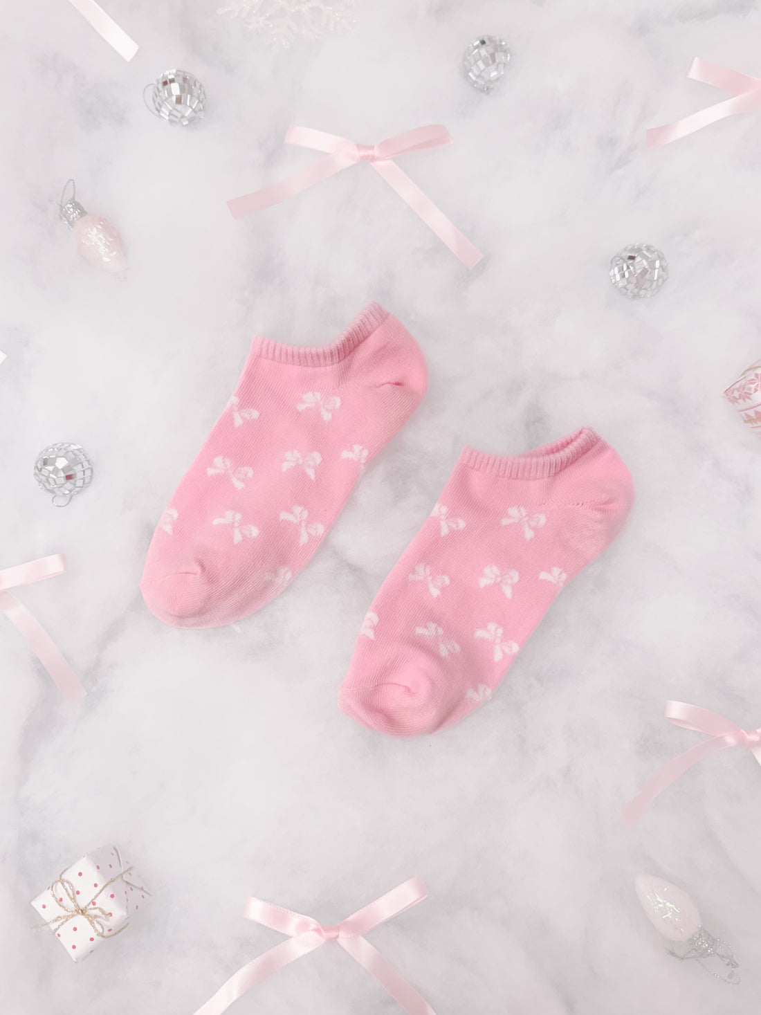 Pink bow-patterned ankle socks arranged on marble with festive ribbons and ornaments.
