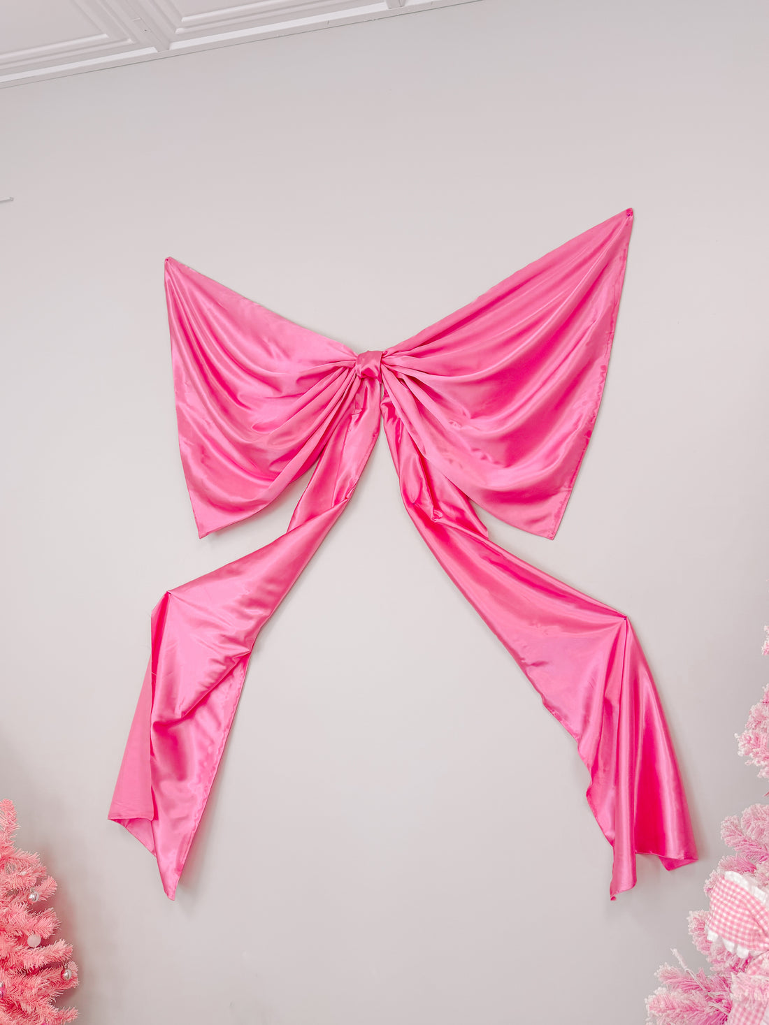Hot pink satin wall bow decoration, draped elegantly against a light grey wall.
