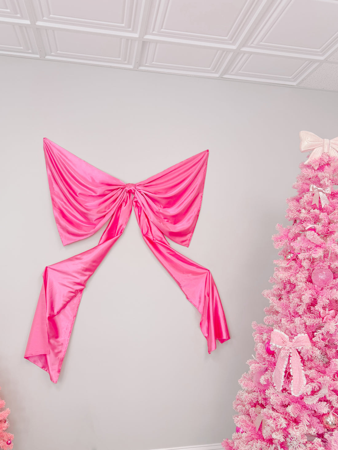 Large hot pink satin bow on a wall, next to a pink Christmas tree.
