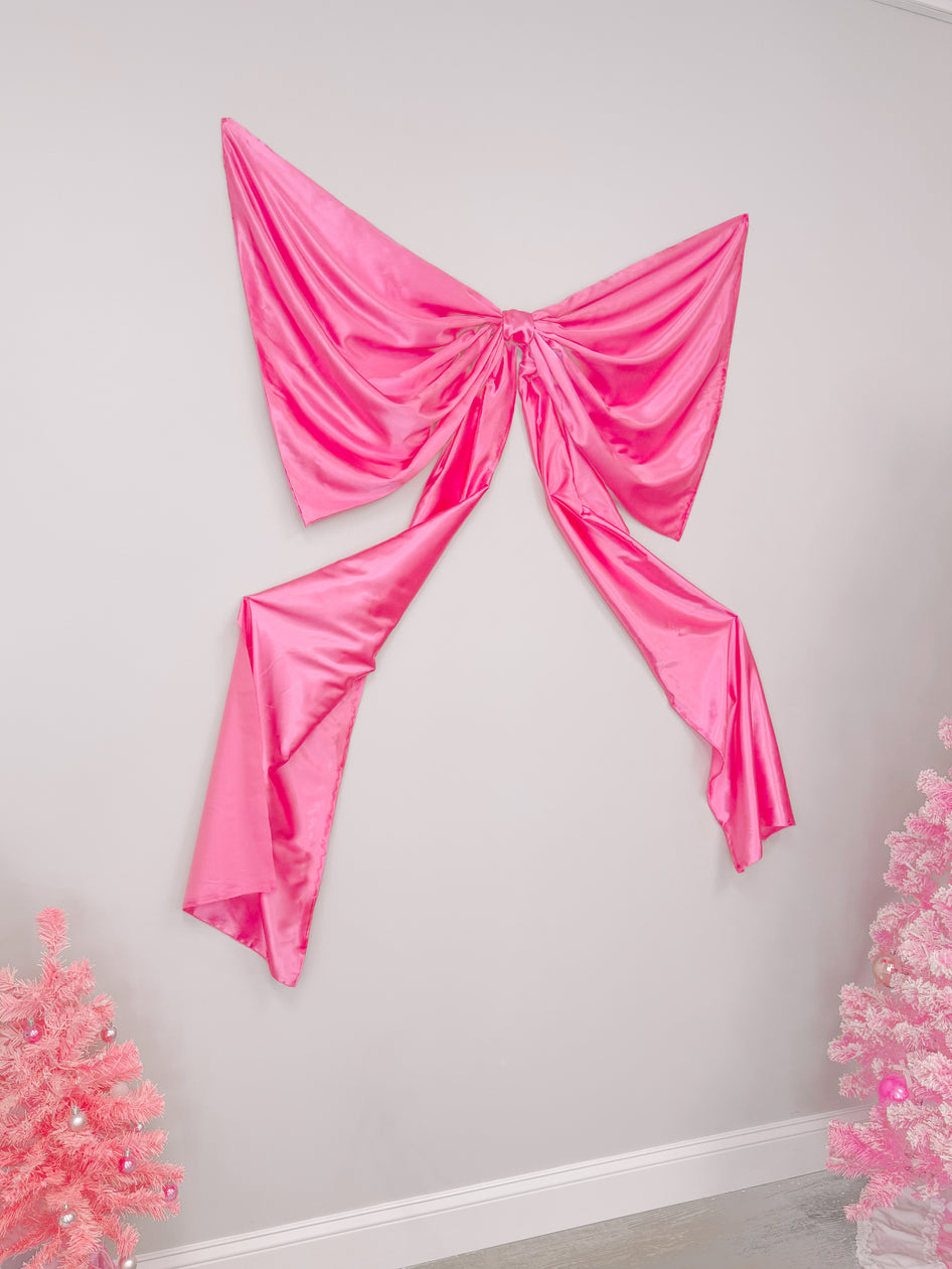 Large pink satin bow wall décor; festive room accent.
