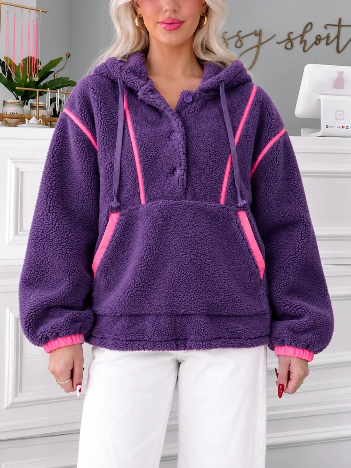 Model wearing the Sassy Shortcake Plum Pretty Pullover, a purple sherpa fleece hoodie with hot pink trim, front pocket and white pants.