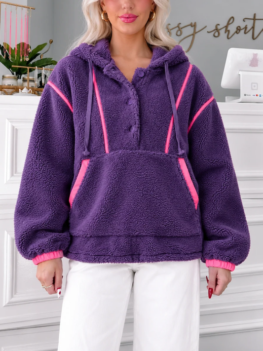 Model wearing the Sassy Shortcake Plum Pretty Pullover, a purple sherpa fleece hoodie with hot pink trim, front pocket and white pants.
