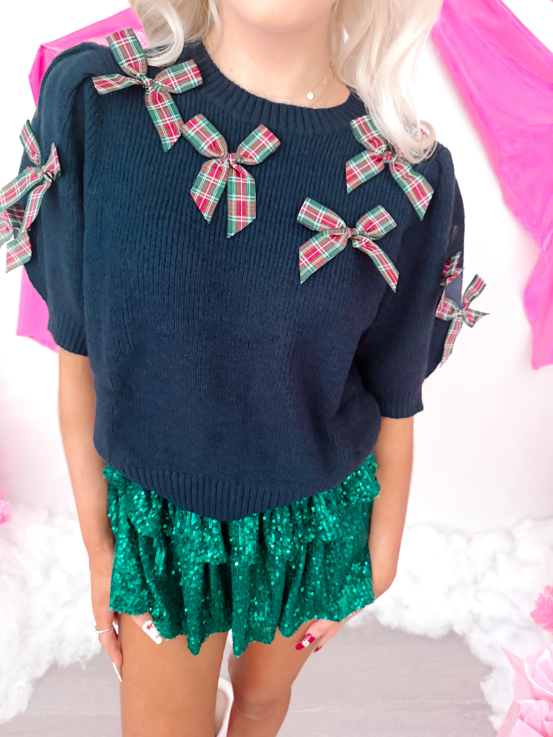 Dark navy blue knit sweater adorned with festive plaid bows, modeled with a sparkly green skirt.
