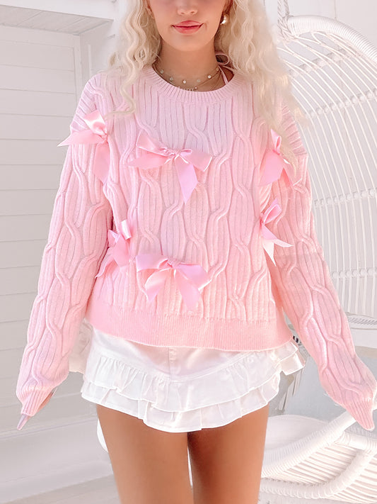 Light pink cable knit sweater with satin bows, modeled against a white background.