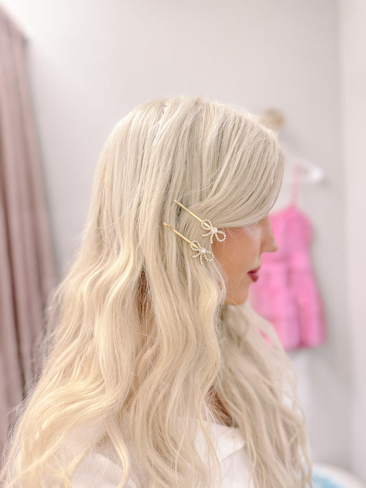 Gold barrette set with sparkling rhinestone bows, in blonde hair.