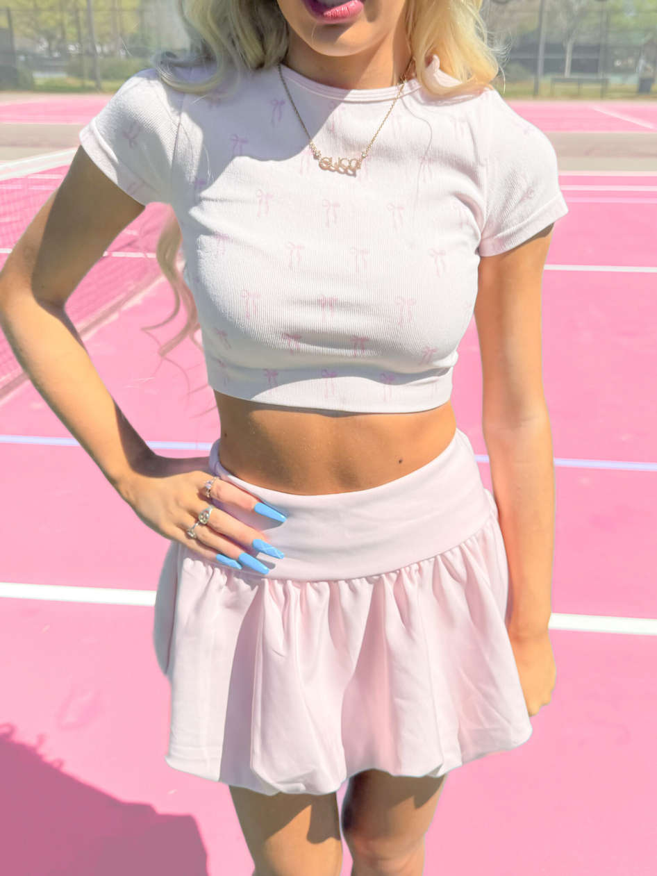White ribbed crop top and mini skirt set with pink bow print.

