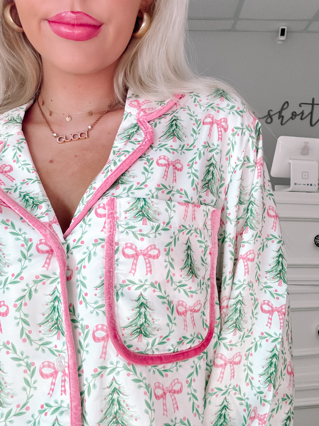Close-up of festive pajama top; pink velvet trim accents a white background with green trees and pink bows from Sassy Shortcake
