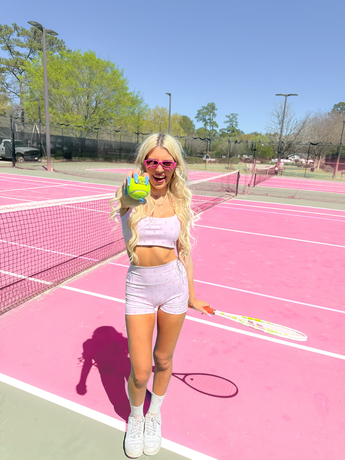 Woman in pink tennis outfit on a pink court, holding a tennis ball and racket.
