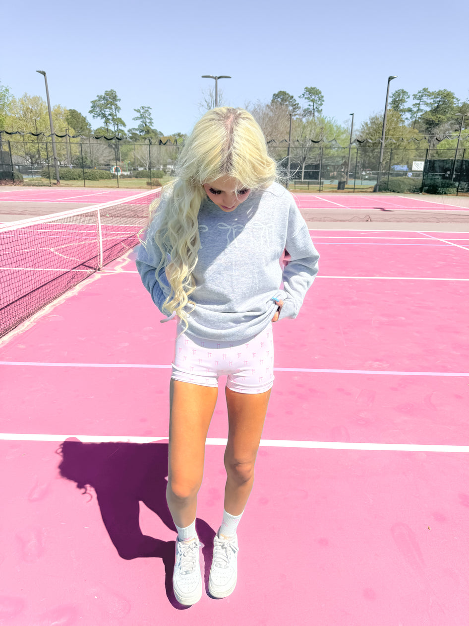 Pink biker shorts with bow print, worn outdoors on a tennis court.
