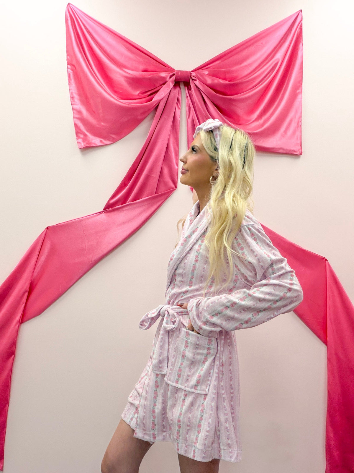 Rose Floral Robe from Sassy Shortcake - Woman in a pink robe standing in front of pink fabric draped like a bow on a wall.