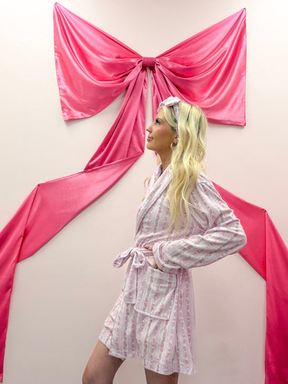 Rose Floral Robe from Sassy Shortcake - Woman in a pink robe standing in front of pink fabric draped like a bow on a wall.