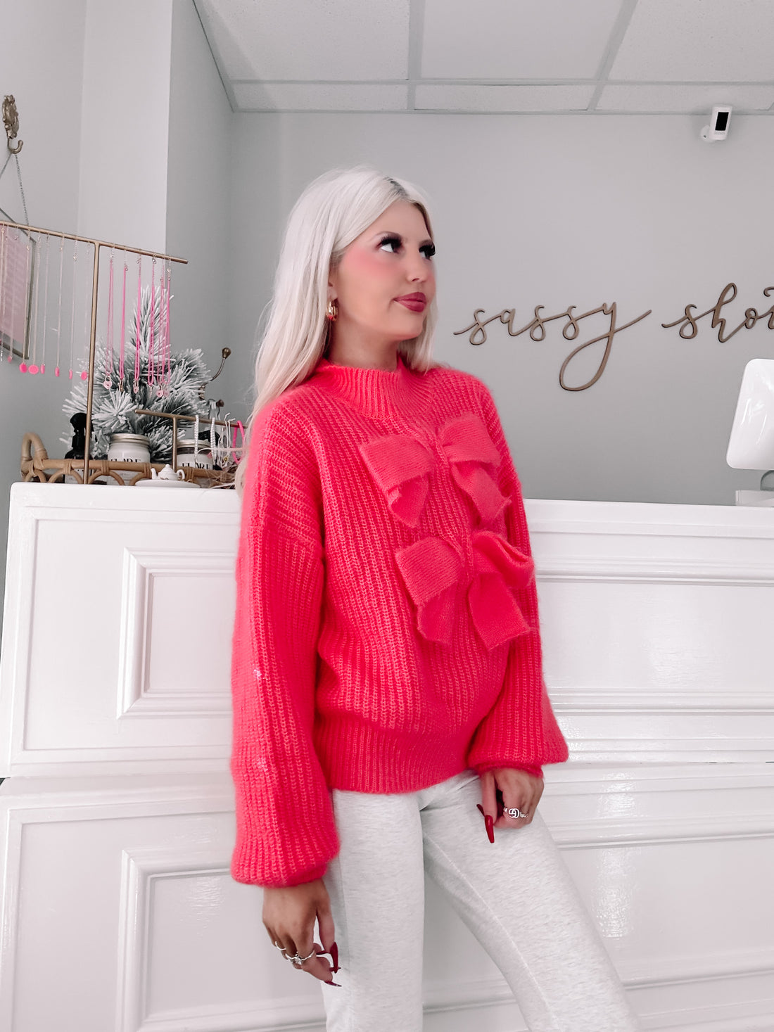 Hot pink knit sweater featuring oversized bows, modeled against a white wall.
