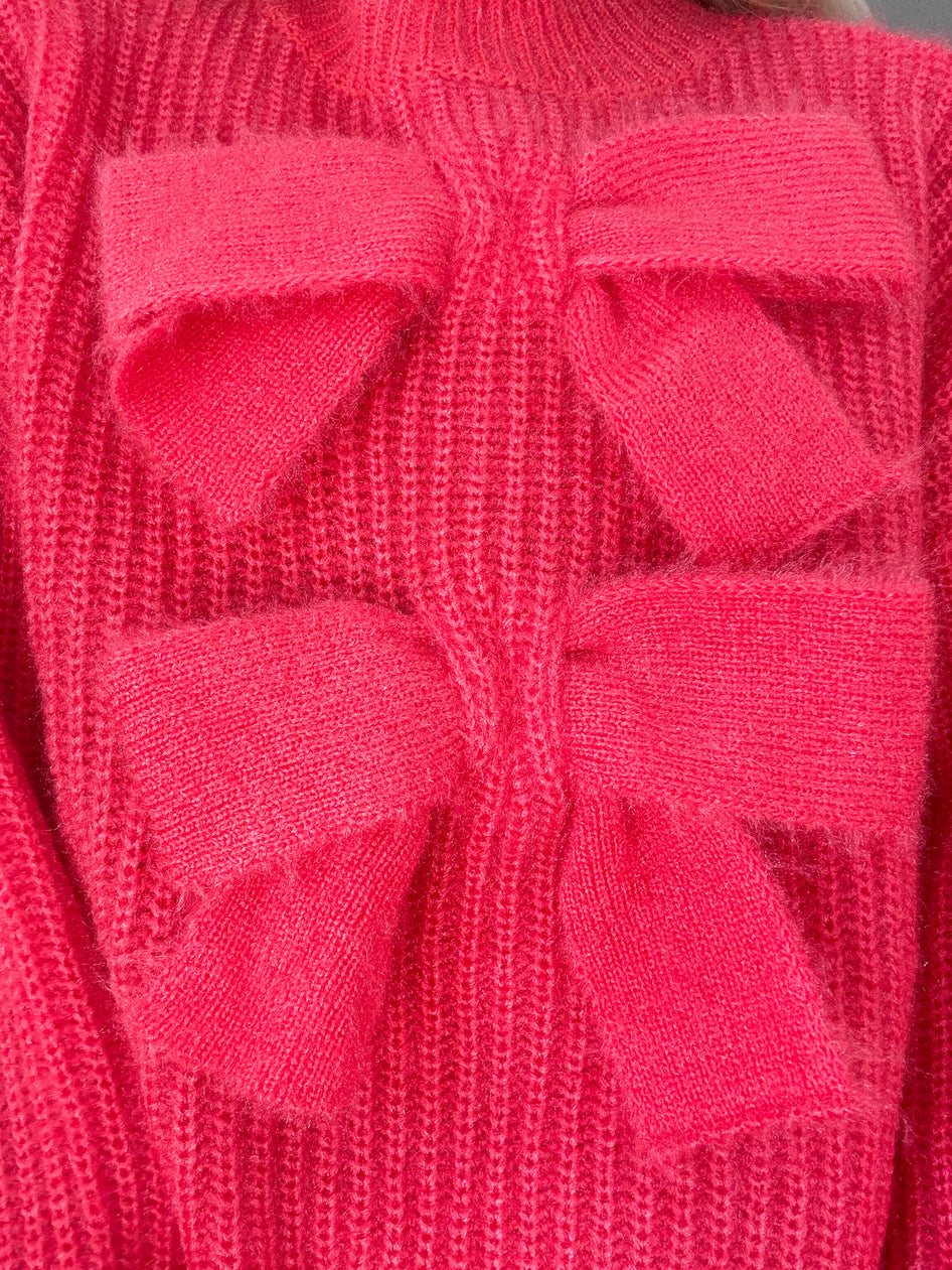 Close-up of a vibrant red knit sweater featuring a large, textured bow detail.
