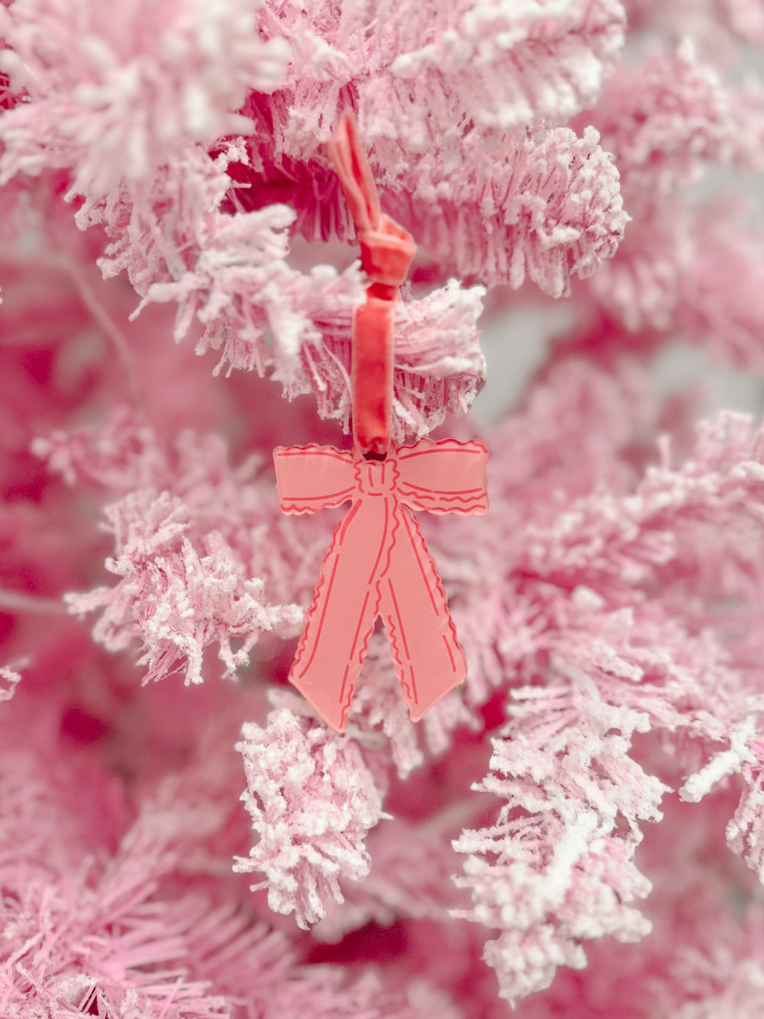 Pink ruffle bow ornament hanging on a flocked pink Christmas tree.
