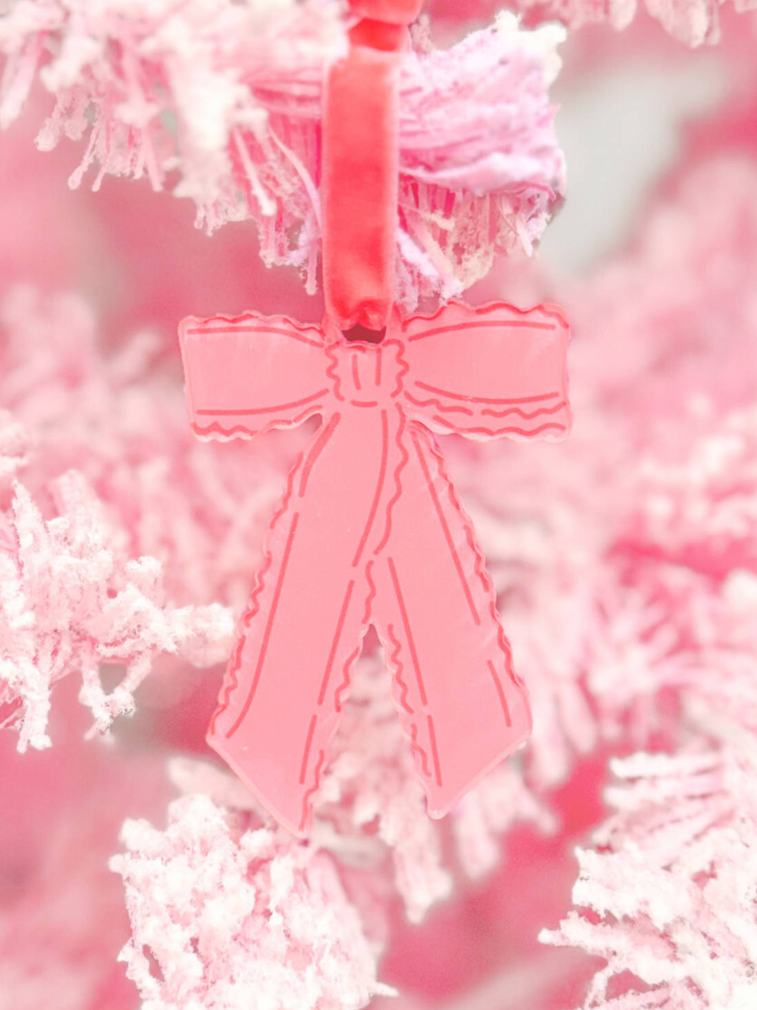 Pink ruffle bow ornament hanging on a pink flocked artificial Christmas tree.
