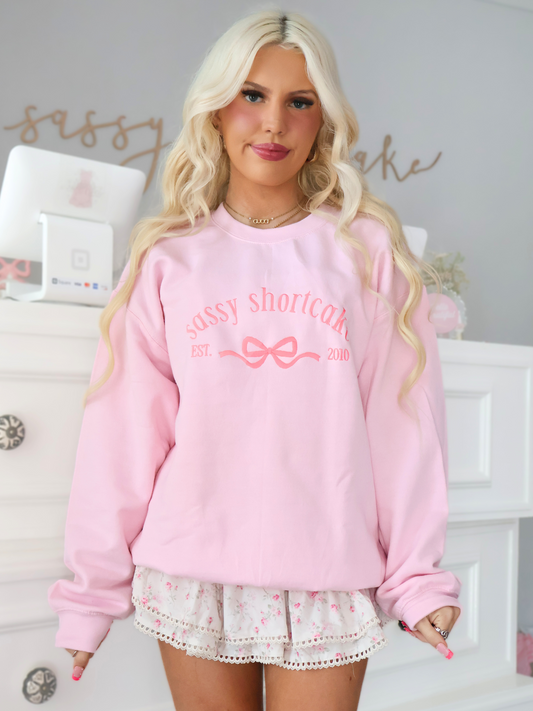 model wearing a pink bow crewneck that says sassy shortcake on the front