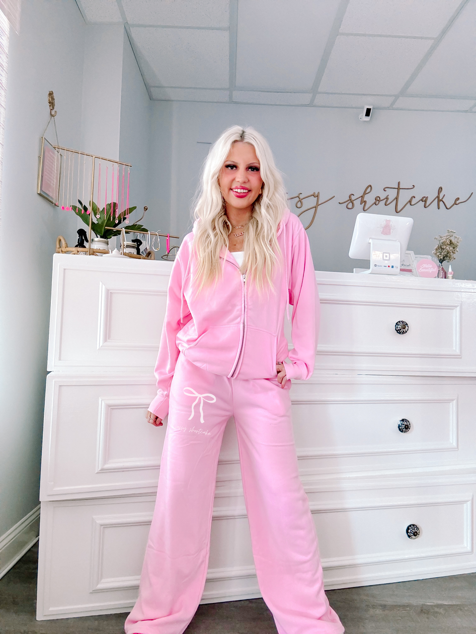 Bubblegum pink wide-leg sweatpants with bow detail, modeled in a boutique.
