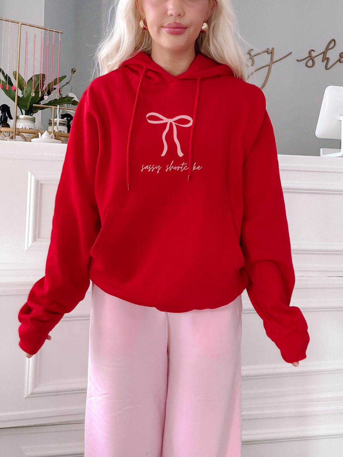 Red hoodie with pink bow design, modeled against a white background.
