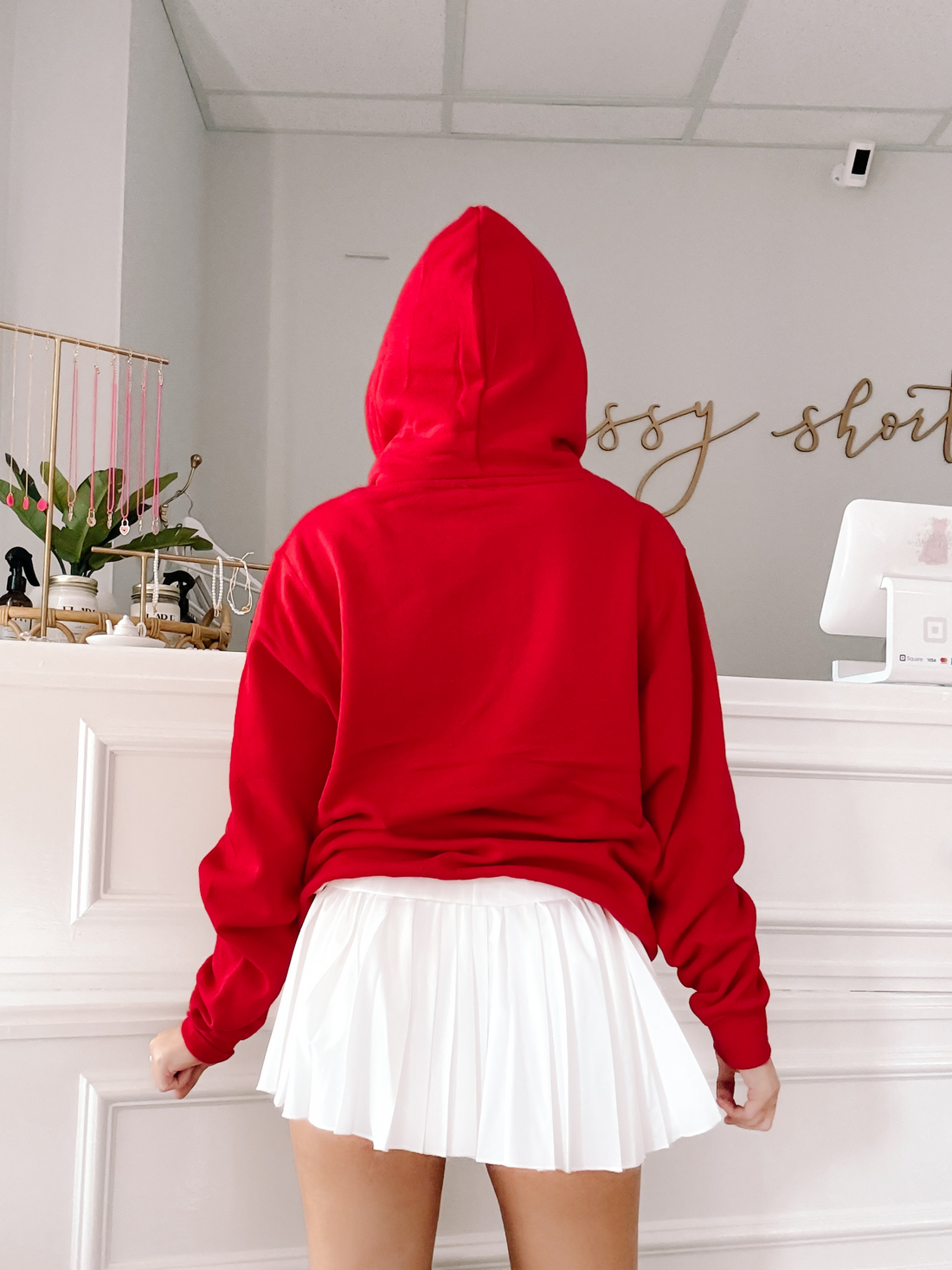 Red hoodie and white pleated skirt, styled in a shop.
