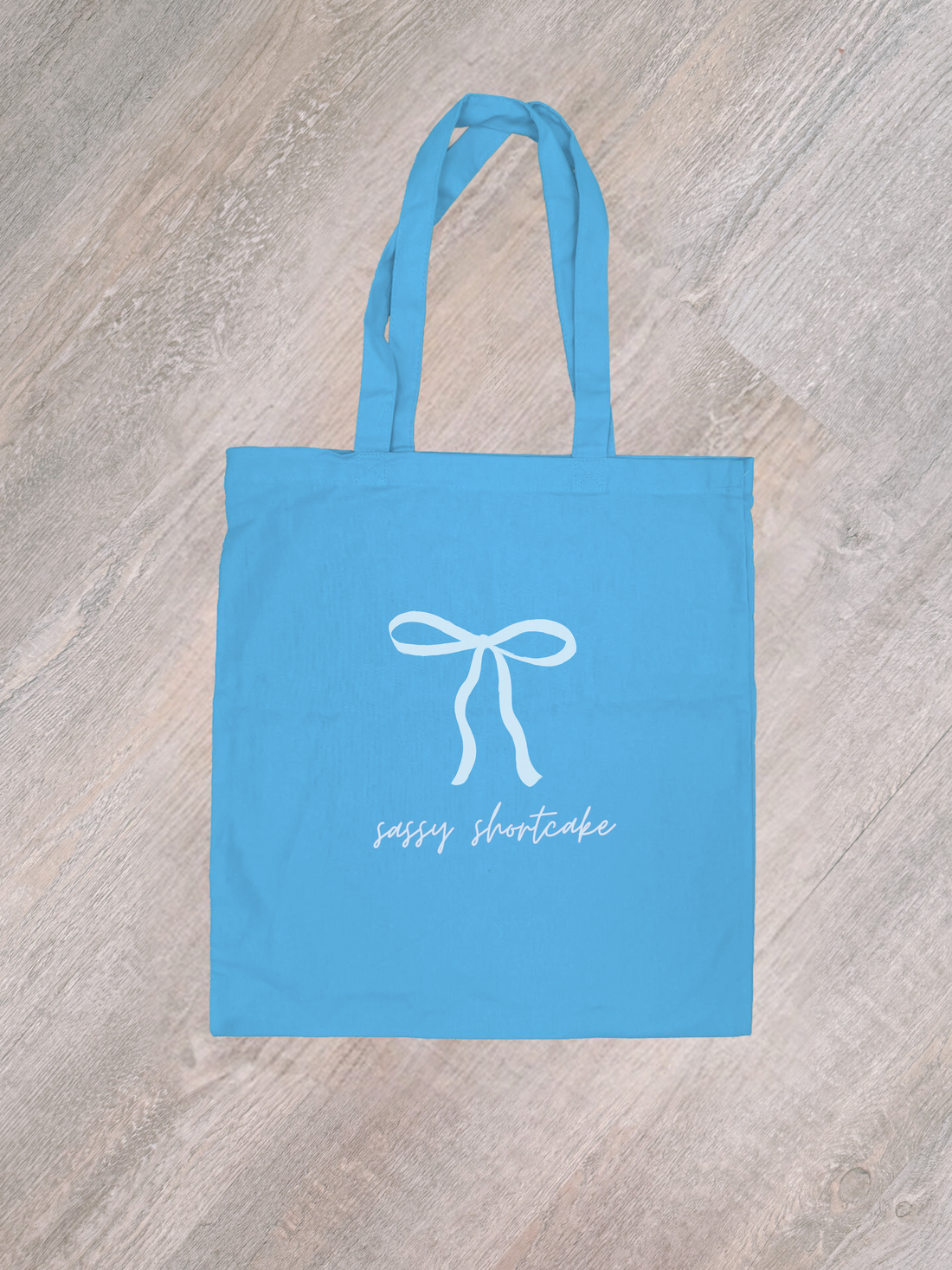 Sky blue cotton tote bag with white bow & "Sassy Shortcake" text.
