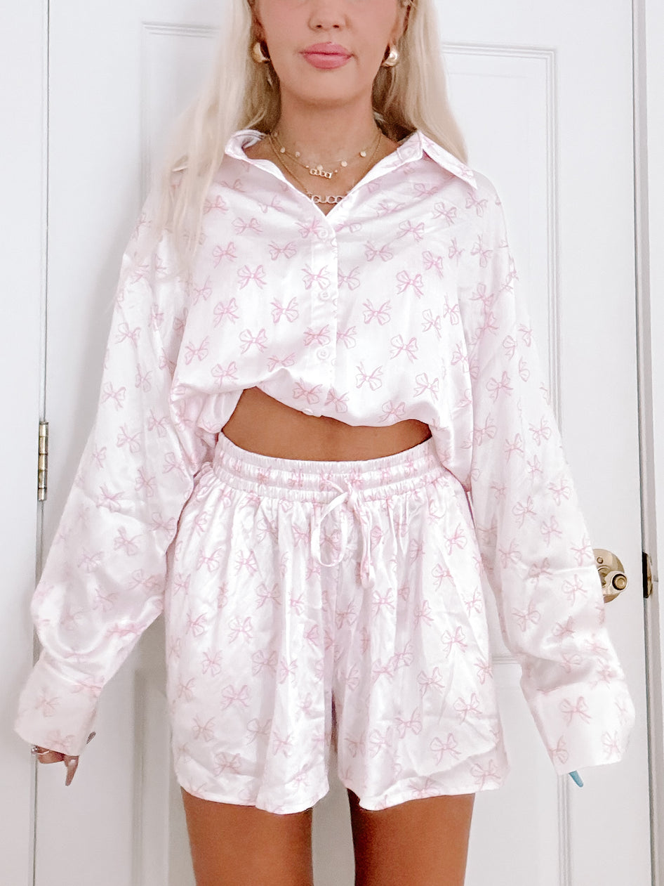 Satin Bow PJ Set: Pink bow print pajama set, featuring a relaxed button-down shirt and shorts.
