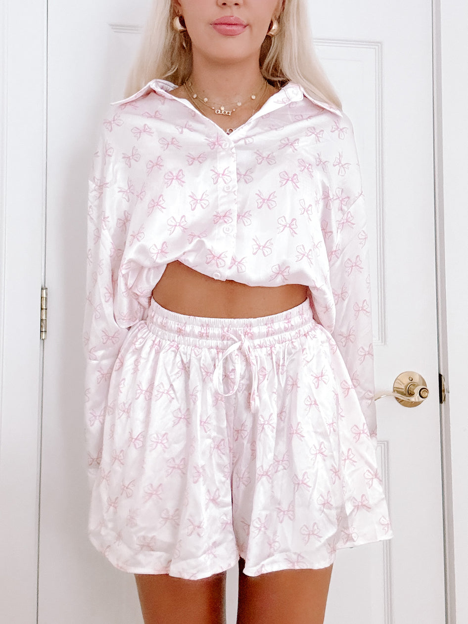Pink satin pajama set with delicate bow print, shown on a model.

