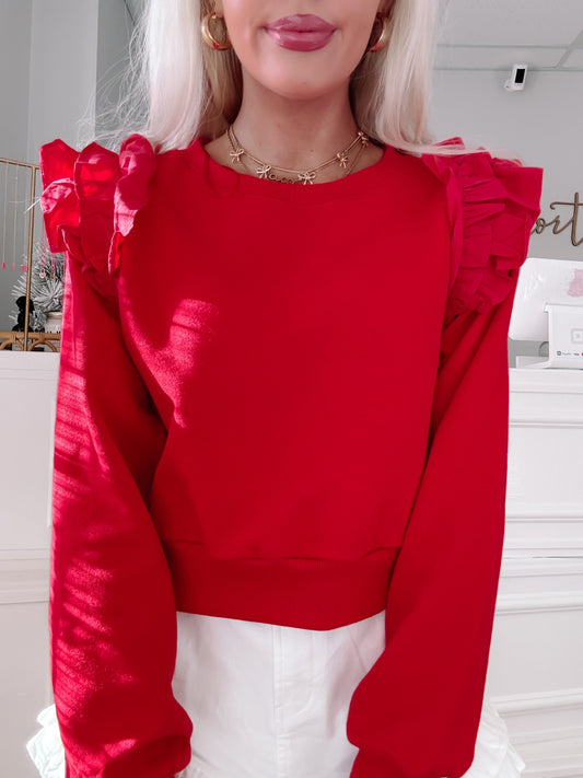 Red cropped sweatshirt with ruffled shoulders, styled with white shorts.