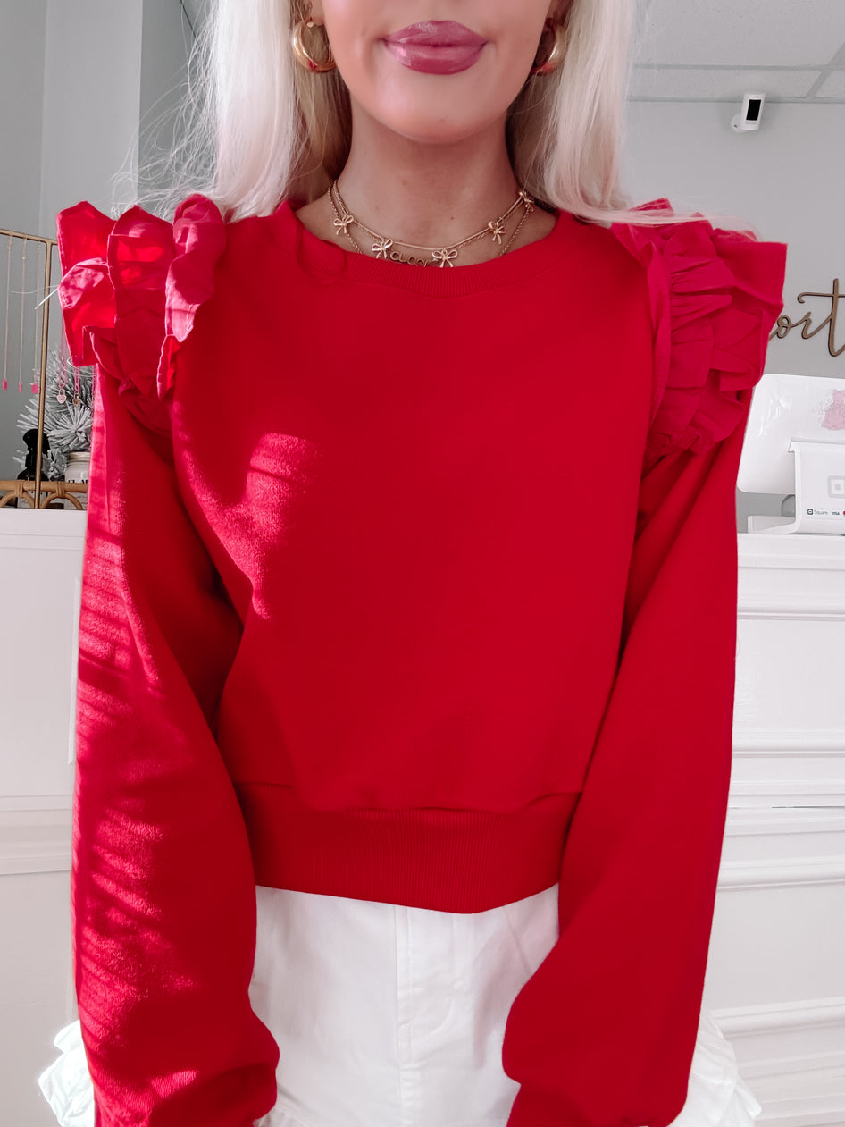 Red cropped sweatshirt with ruffled shoulders, styled with white shorts.
