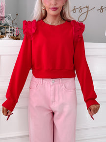 Red cropped sweatshirt with ruffled shoulders, modeled with pink pants.
