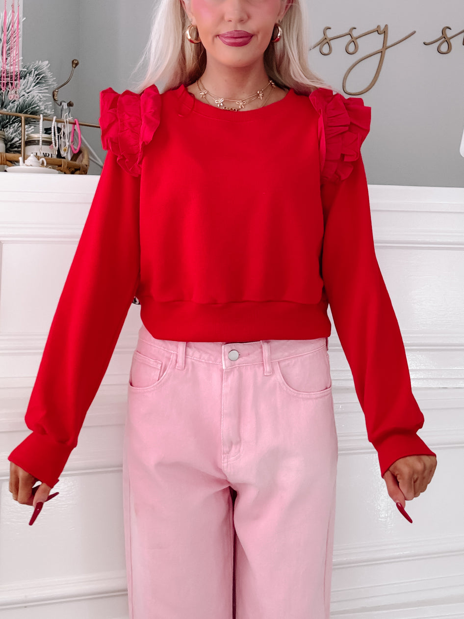 Red cropped sweatshirt with ruffled shoulders, modeled with pink pants.
