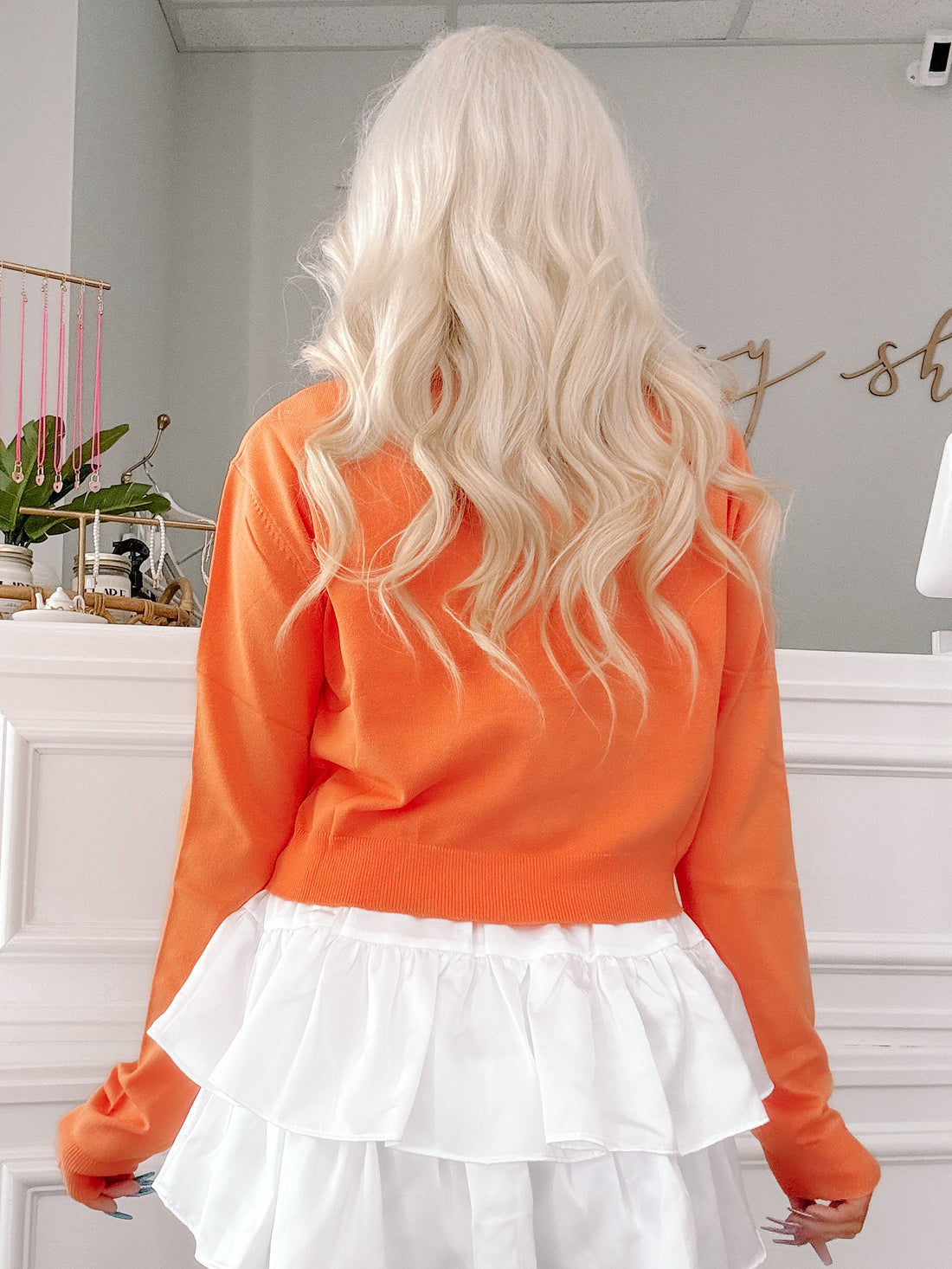 Bright orange cropped cardigan with a layered white ruffle skirt detail.
