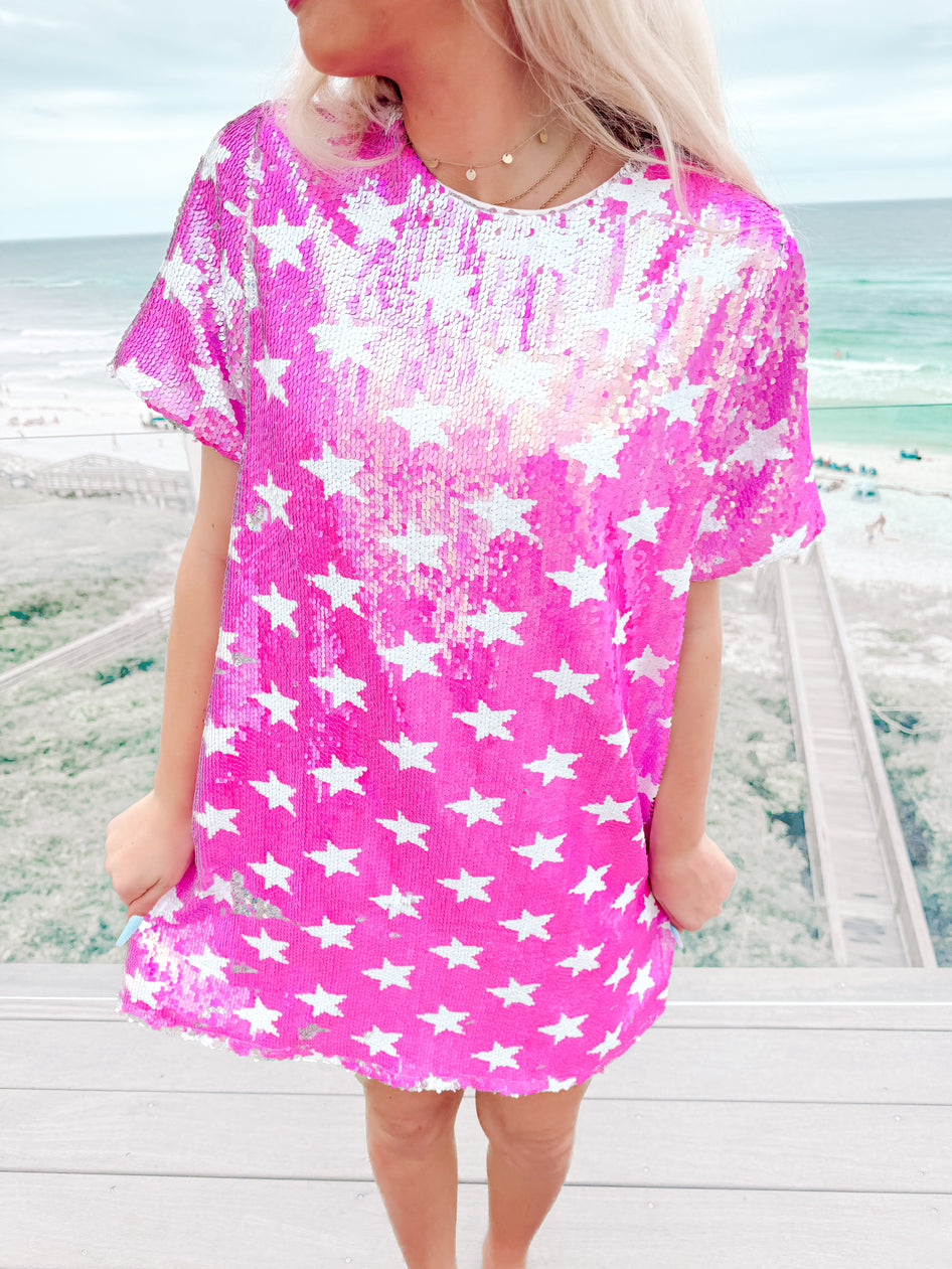 Sequin mini dress with white stars, shown outdoors on a deck overlooking the ocean.
