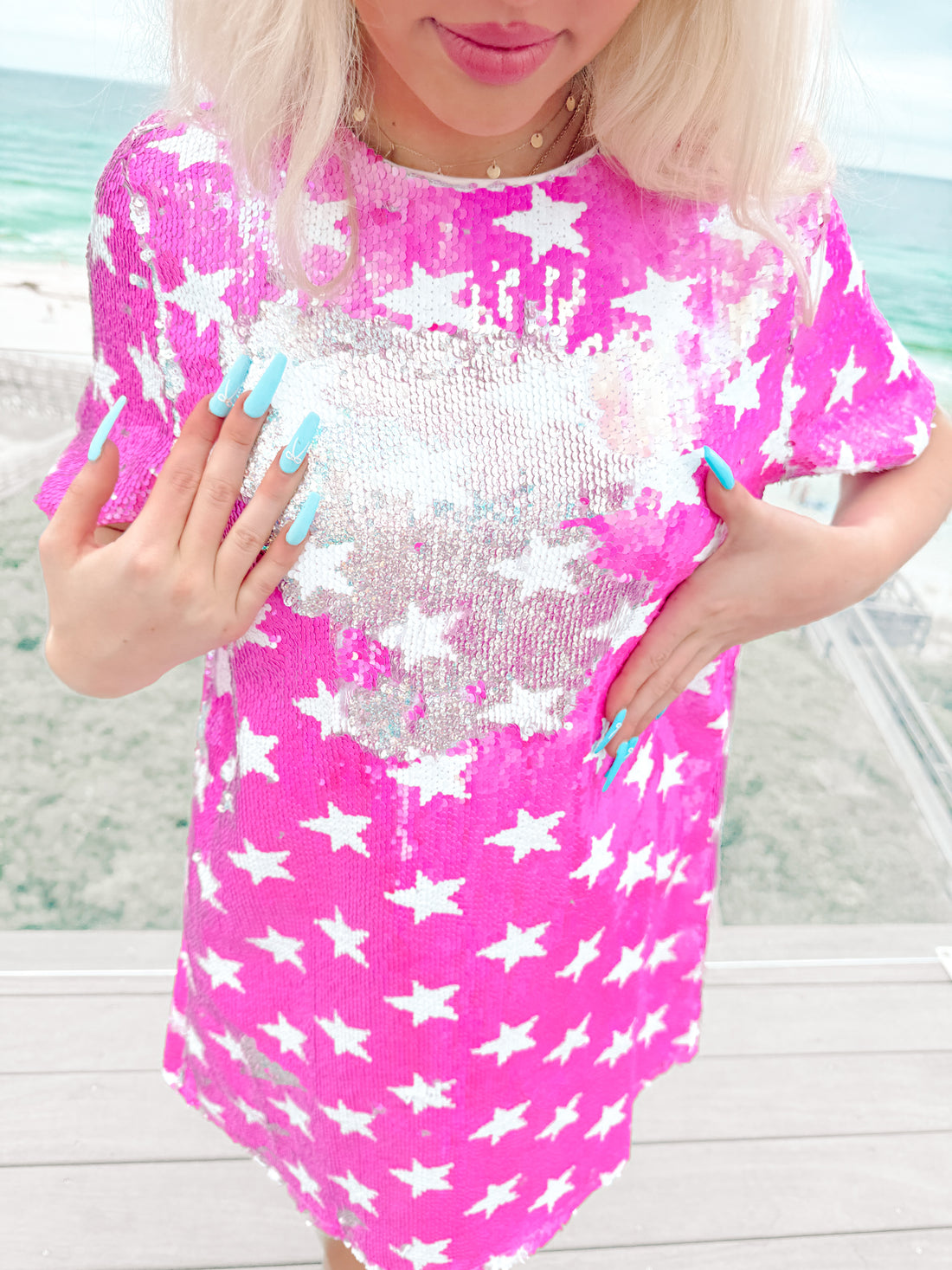 Pink sequin mini dress with white star pattern, shown outdoors near the ocean.
