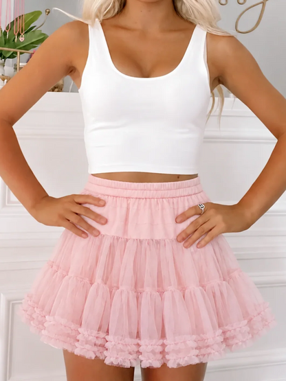 Model wearing the Sugar Plum Skirt from Sassy Shortcake, a blush pink tiered tulle mini skirt with ruffle trim and an elastic waist, styled with a white crop tank clara top.