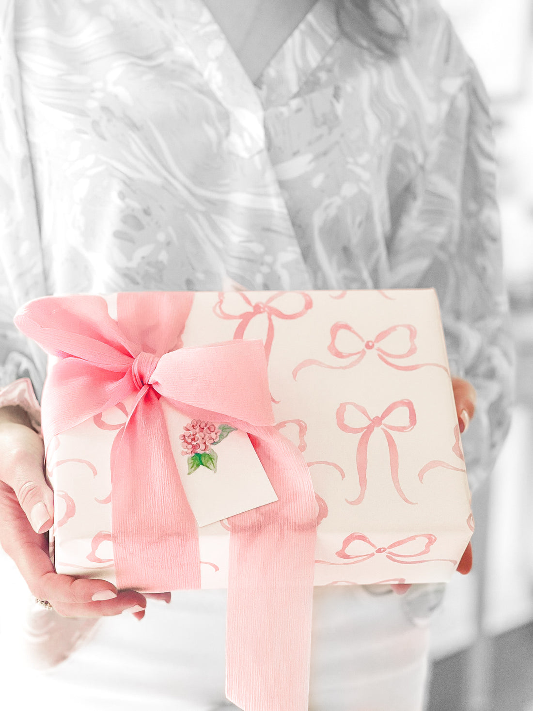 Gift box with pink ribbon and bow, delicate watercolor bow print, presented in hands.
