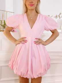 Pink bubble mini dress with puff sleeves and V-neckline, modeled against a white background.
