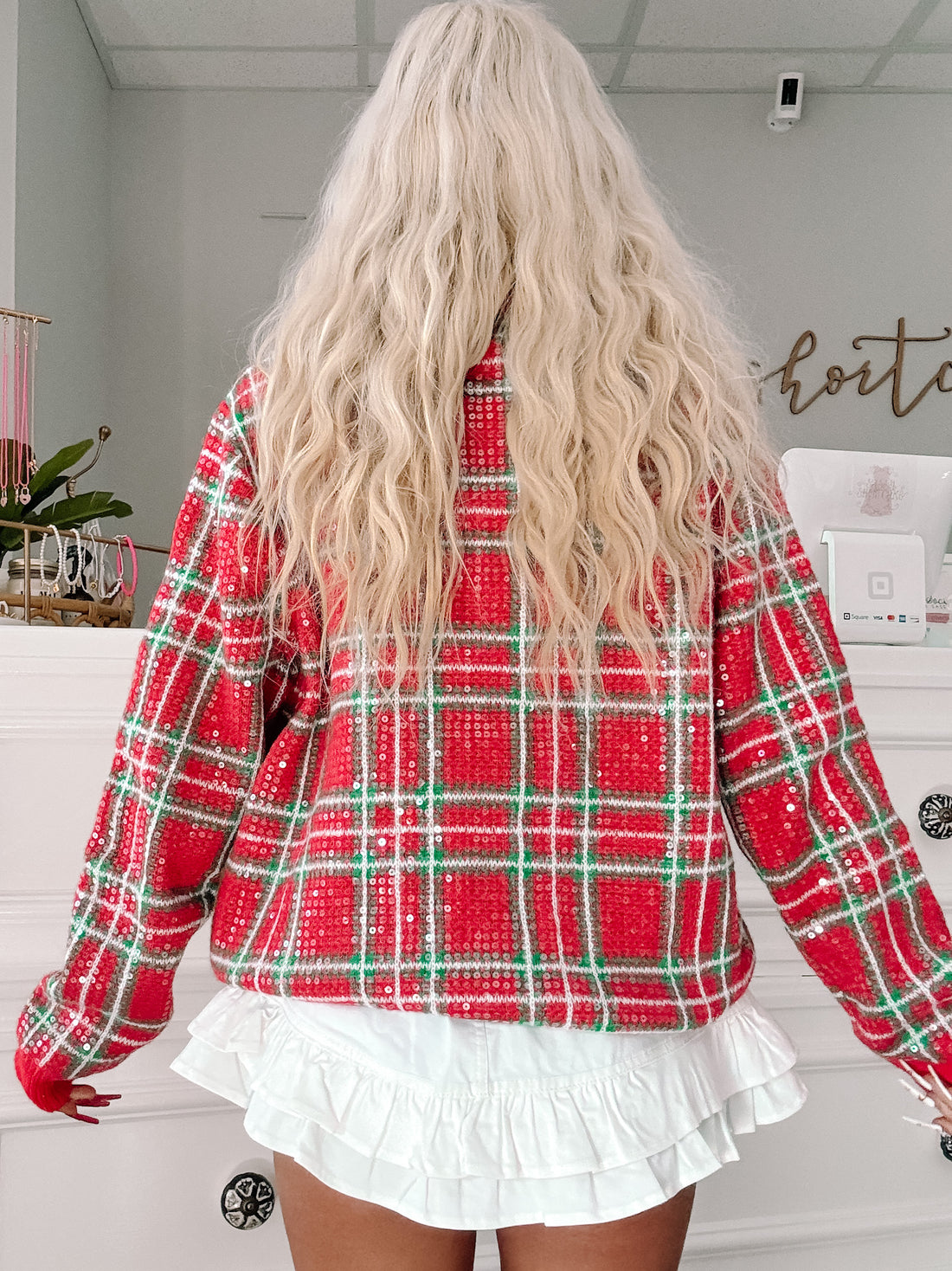 Red and green sequined plaid sweater, shown from the back, paired with a white ruffled skirt.
