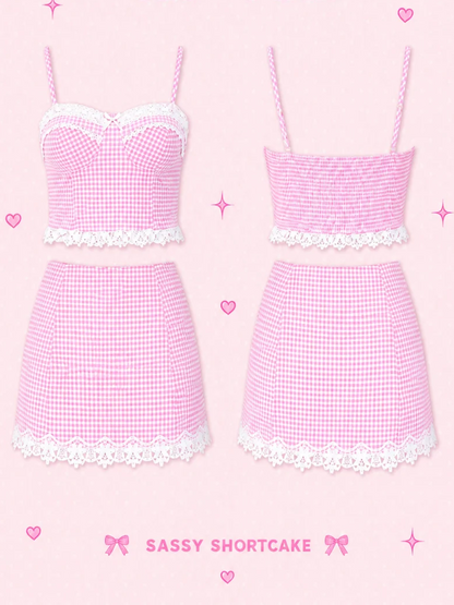 Pink gingham two-piece outfits shown on a light pink background with decorative text reading 'SWEET ON GINGHAM SET - PINK' and 'Sassy Shortcake'. The set includes a strapless crop top with white lace trim and a matching mini skirt, shown in two colorways: one solid pink and one pink-and-white gingham. Sweet on Gingham Outfit Set - New Arrival