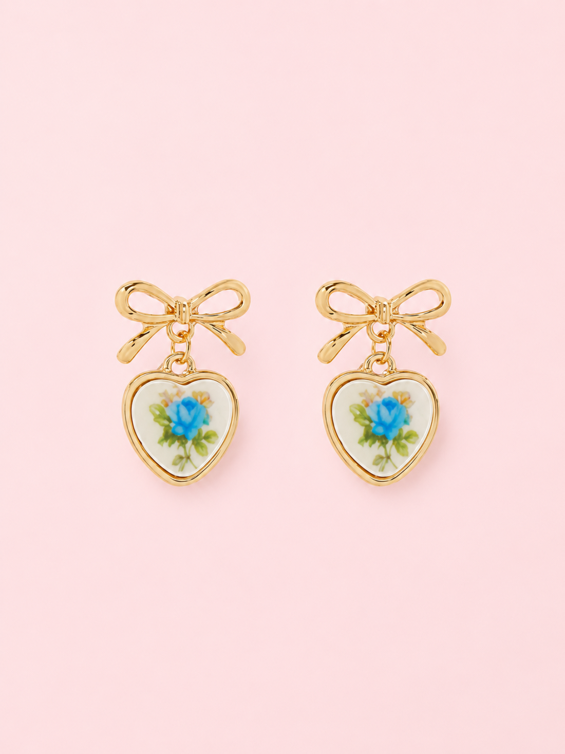 Sweet Bloom Bow Earrings in Blue from Sassy Shortcake: Gold bow earrings with ceramic heart charms featuring a blue rose print on a light pink background.