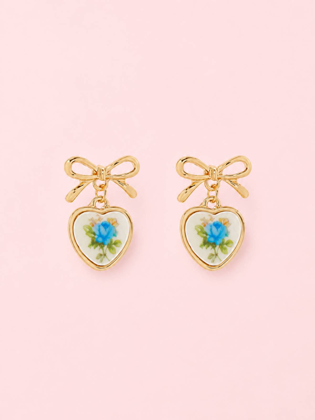 Sweet Bloom Bow Earrings in Blue from Sassy Shortcake: Gold bow earrings with ceramic heart charms featuring a blue rose print on a light pink background.
