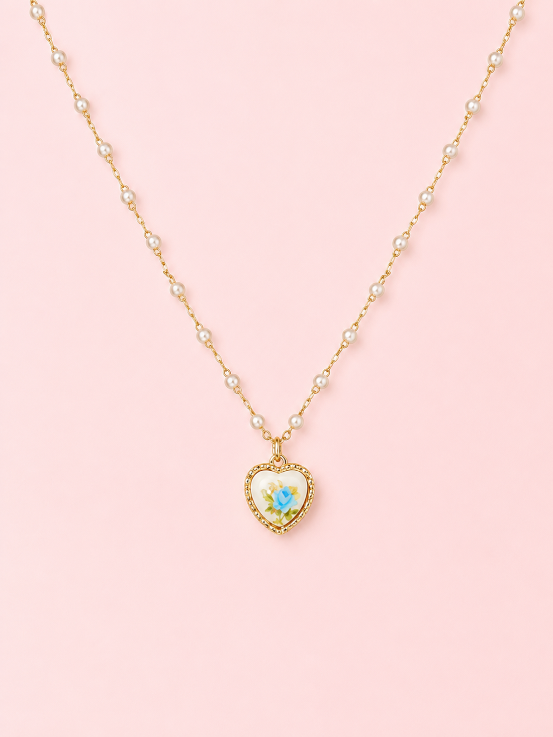 Sweet Bloom Bow Necklace in Blue from Sassy Shortcake featuring a gold-tone pearl-accent chain with a heart charm and blue rose print on a light pink background.