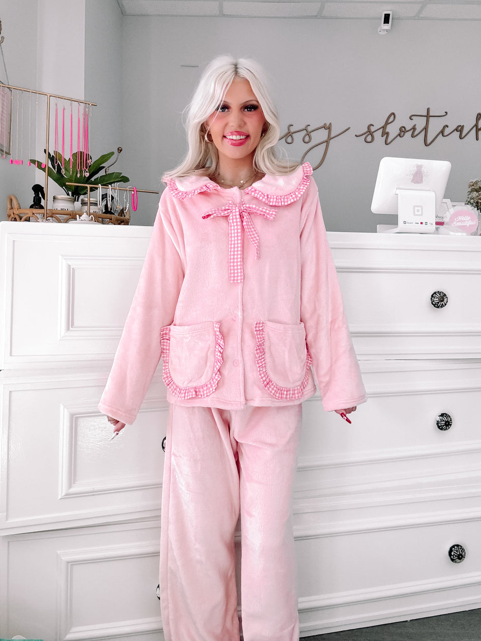 Pink plush pajama set with gingham trim, modeled in a boutique setting.
