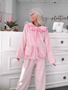 Pink plush pajama set with gingham trim, modeled in a boutique.
